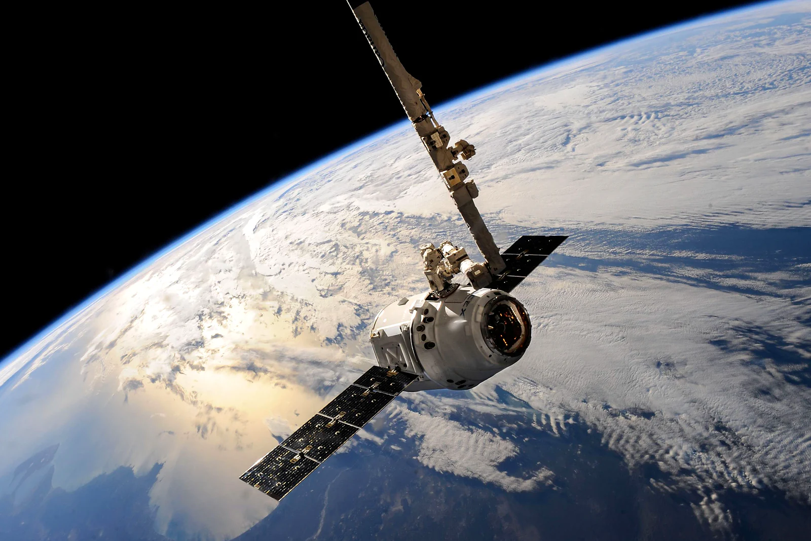 A cargo spacecraft held by the space station's robotic arm above Earth